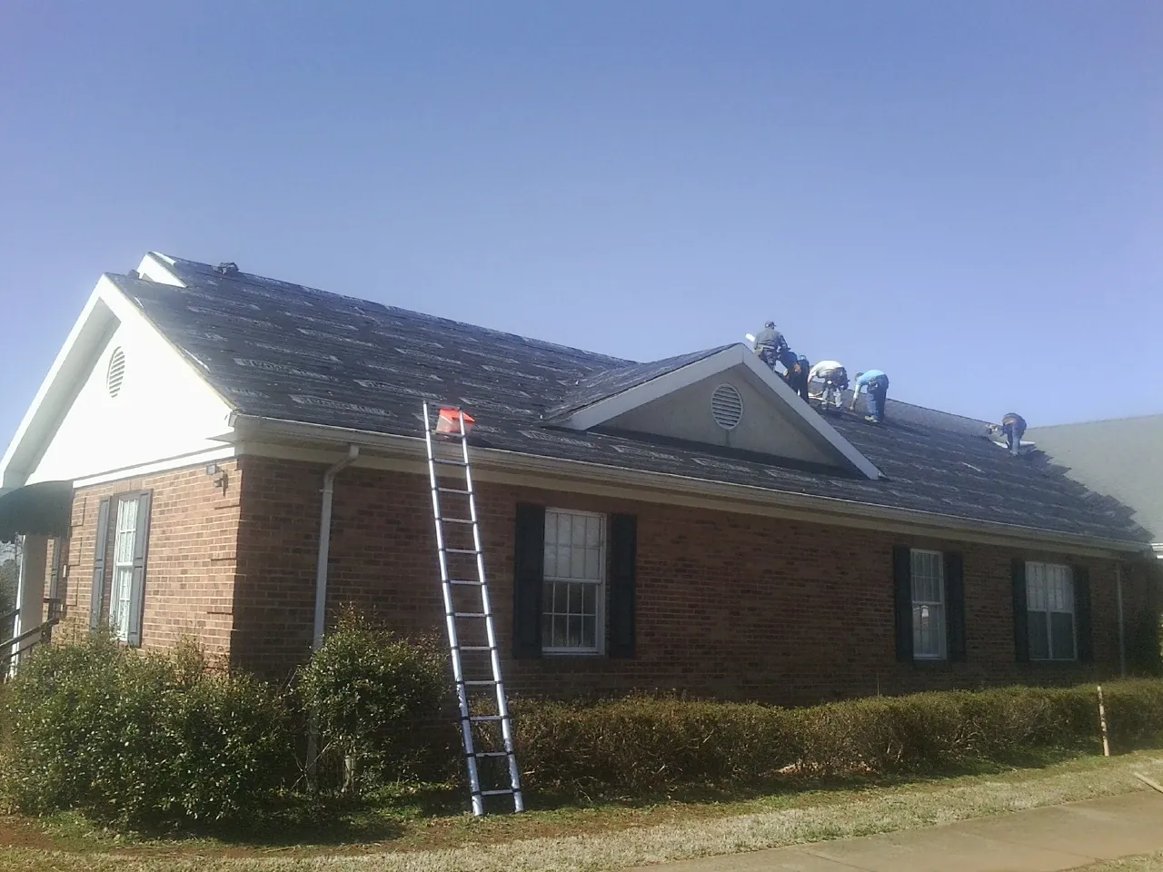 Crew tearing shingles off a brick ranch roof with a ladder set — Emergency Roof Repair work by our crew in Yeagertown