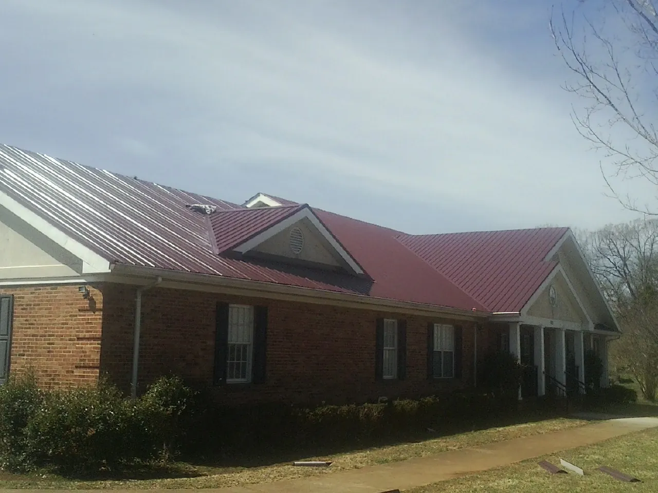 Red metal roof with gabled entries on a long brick building, from a Hail Damage Roof Repair job in Yeagertown