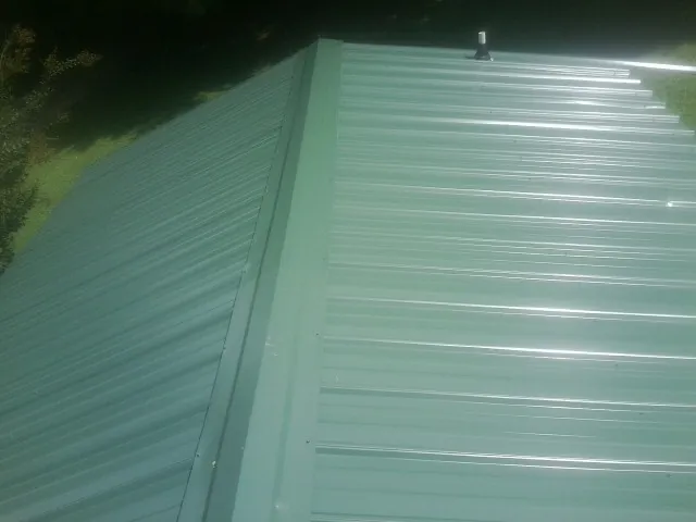 New green metal panels meeting at the ridge of a roof — Flat Roof Repair work by our crew in Yeagertown