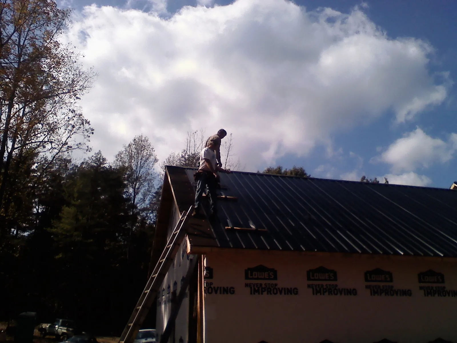 Roofer fastening dark metal panels high against a cloudy sky, from a Roof Inspection job in Yeagertown
