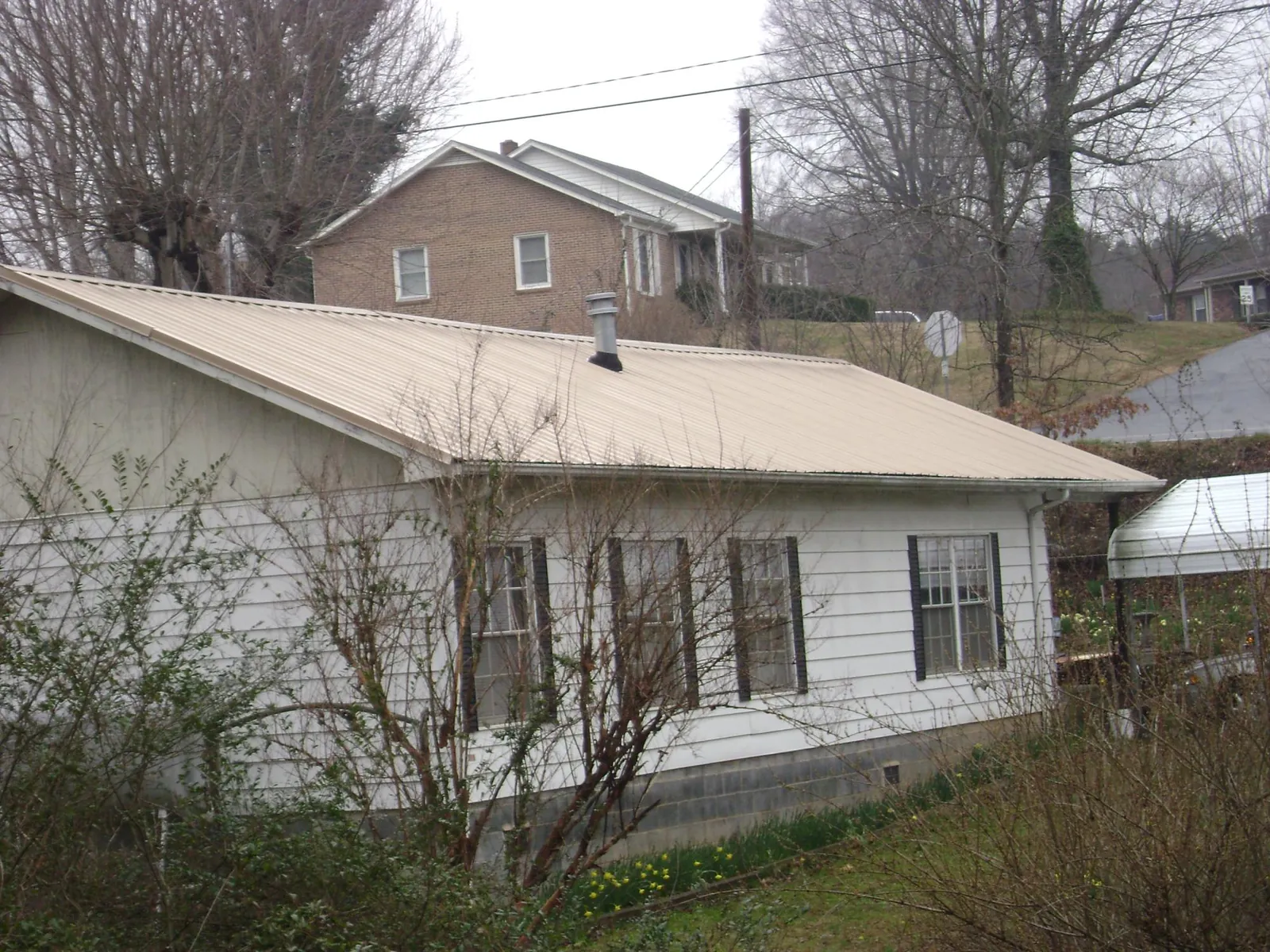 Tan metal roof on a white sided house set into a hillside — Commercial Roofing by Roofing Brothers in Yeagertown